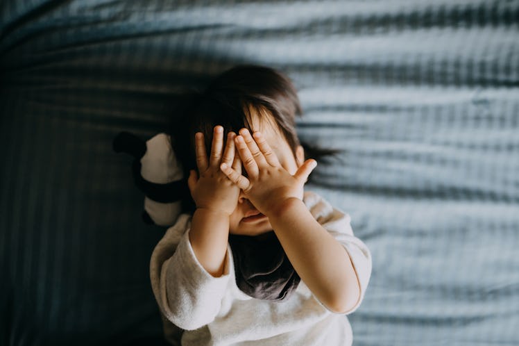 A young girl covers her face with her hands while lying on a bed.