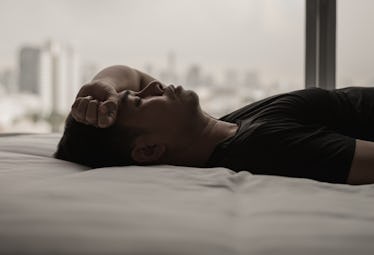 A sad man lies in bed.