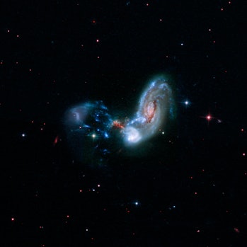image of a disk-shaped galaxy with one disturbed arm and a trail of gas it's subsuming near