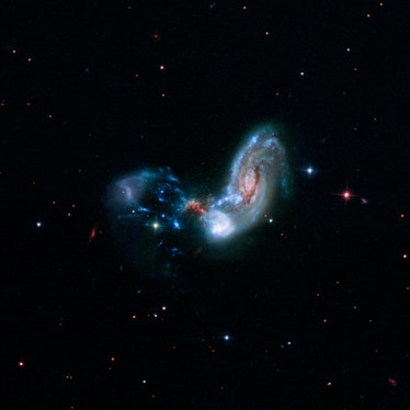 image of a disk-shaped galaxy with one disturbed arm and a trail of gas it's subsuming near