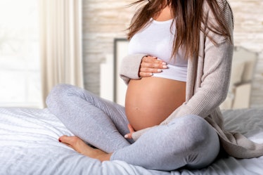 Lower section of a pregnant woman as she sits on a bed, legs criss-crossed.