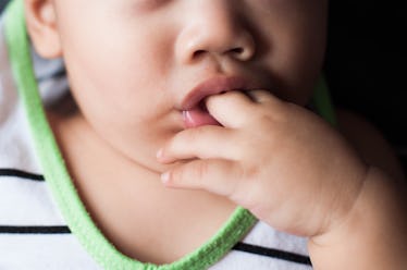 A baby with their fingers in their mouth.