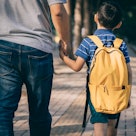 A dad holds his son's hand, walking him to the first day of school.