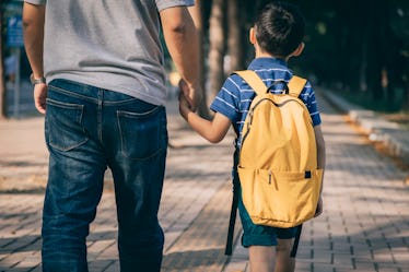 A dad holds his son's hand, walking him to the first day of school.