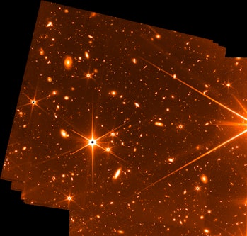 False-color image of stars and distant galaxies in reds, oranges, yellows, and whites.