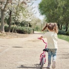 A child walks her bike in the street alone.
