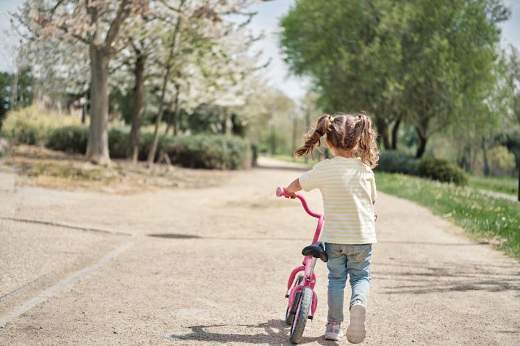 A child walks her bike in the street alone.