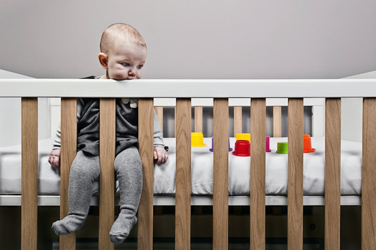 A bored baby sitting in a crib, staring aimlessly.