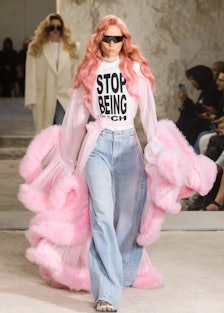 A model walking down the Vetements runway wearing a shirt that reads, "Stop Being Rich"