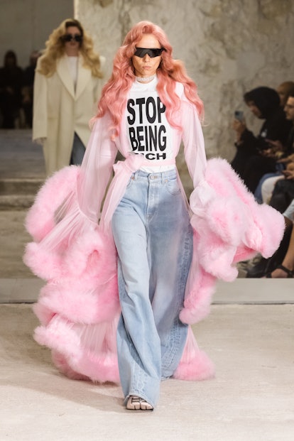 A model walking down the Vetements runway wearing a shirt that reads, "Stop Being Rich"