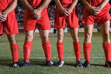 Lower half of male soccer players as they stand in a line with their hands protecting their balls.
