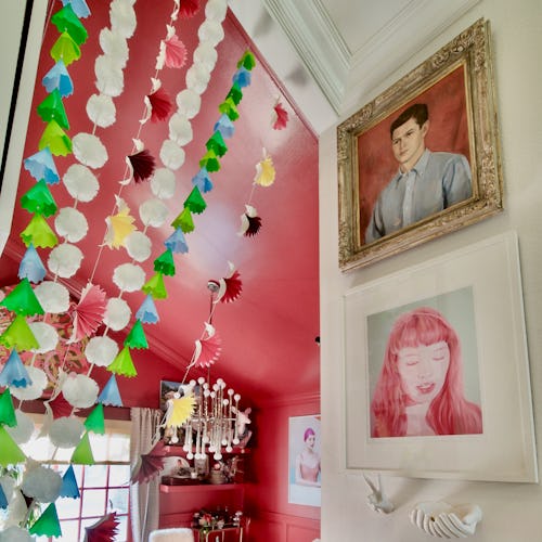 A room with one pink wall, one white wall, pink-tone pictures and green and white decorations
