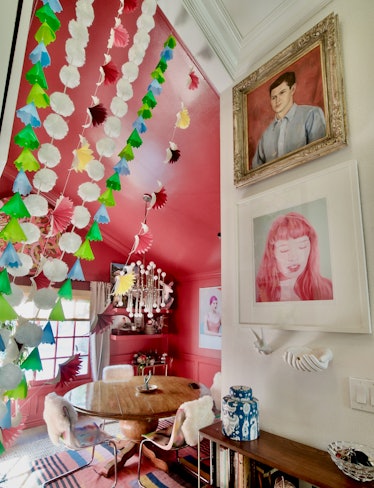 A room with one pink wall, one white wall, pink-tone pictures and green and white decorations