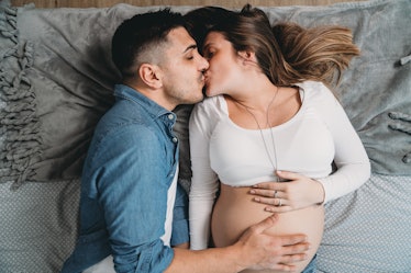 A man and pregnant woman kiss in bed.