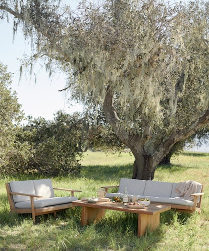 Jenni Kayne's Santa Ynez Ranch Home, benches and chairs with a wooden table sit in the shade of a tr...