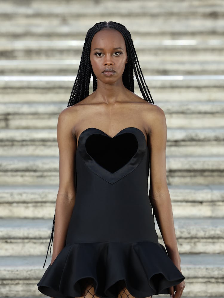 A model walking on the runway in a black mini dress at the Valentino haute couture fall/winter 22/23...