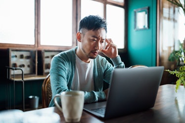 Frustrated asian man looking at laptop with his hand on his head