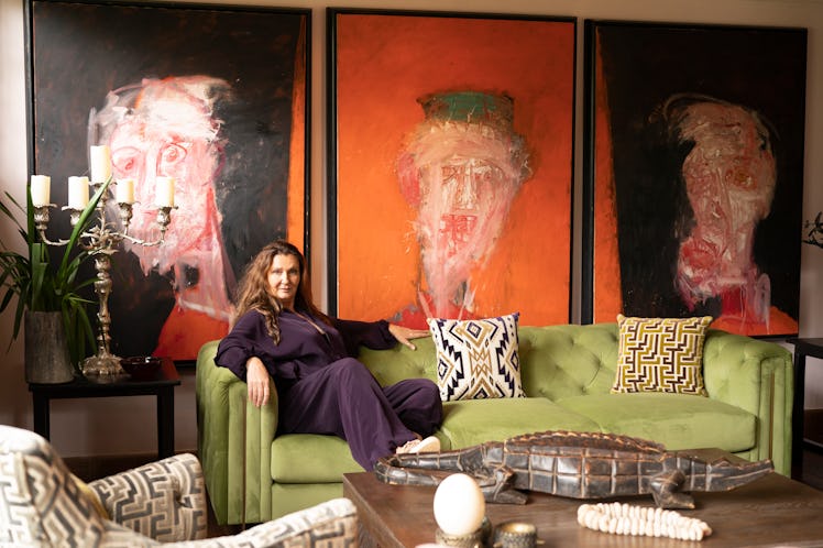 a woman reclines on a green sofa in front of three large paintings