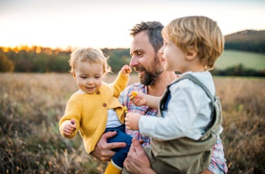 A dad in a field carrying his two kids.