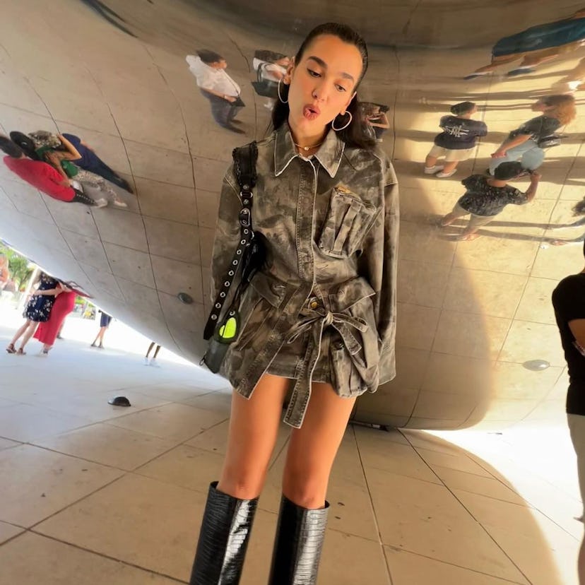 A photo of Dua Lipa standing under the Chicago bean sculpture.