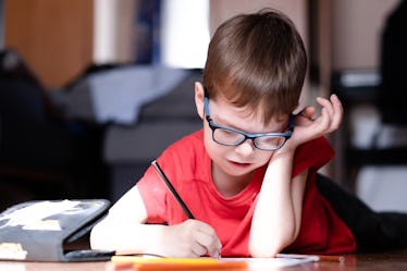 A kindergartener in a red shirt lying on the ground, drawing.