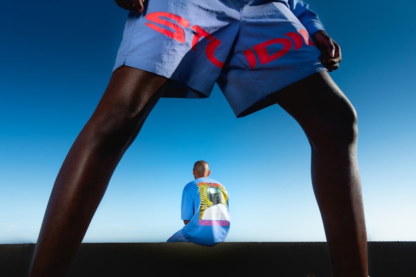 Supervsn Studios Blue shorts with pink text in front and in the background model in blue T-shirt wit...