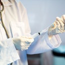 A doctor in a white coat uses a syringe to draw the flu vaccine from a vial.