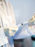 A doctor in a white coat uses a syringe to draw the flu vaccine from a vial.