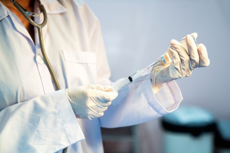 A doctor in a white coat uses a syringe to draw the flu vaccine from a vial.