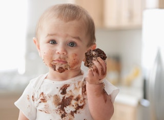 A little baby eating a sweet cookie, all smeared with chocolate.