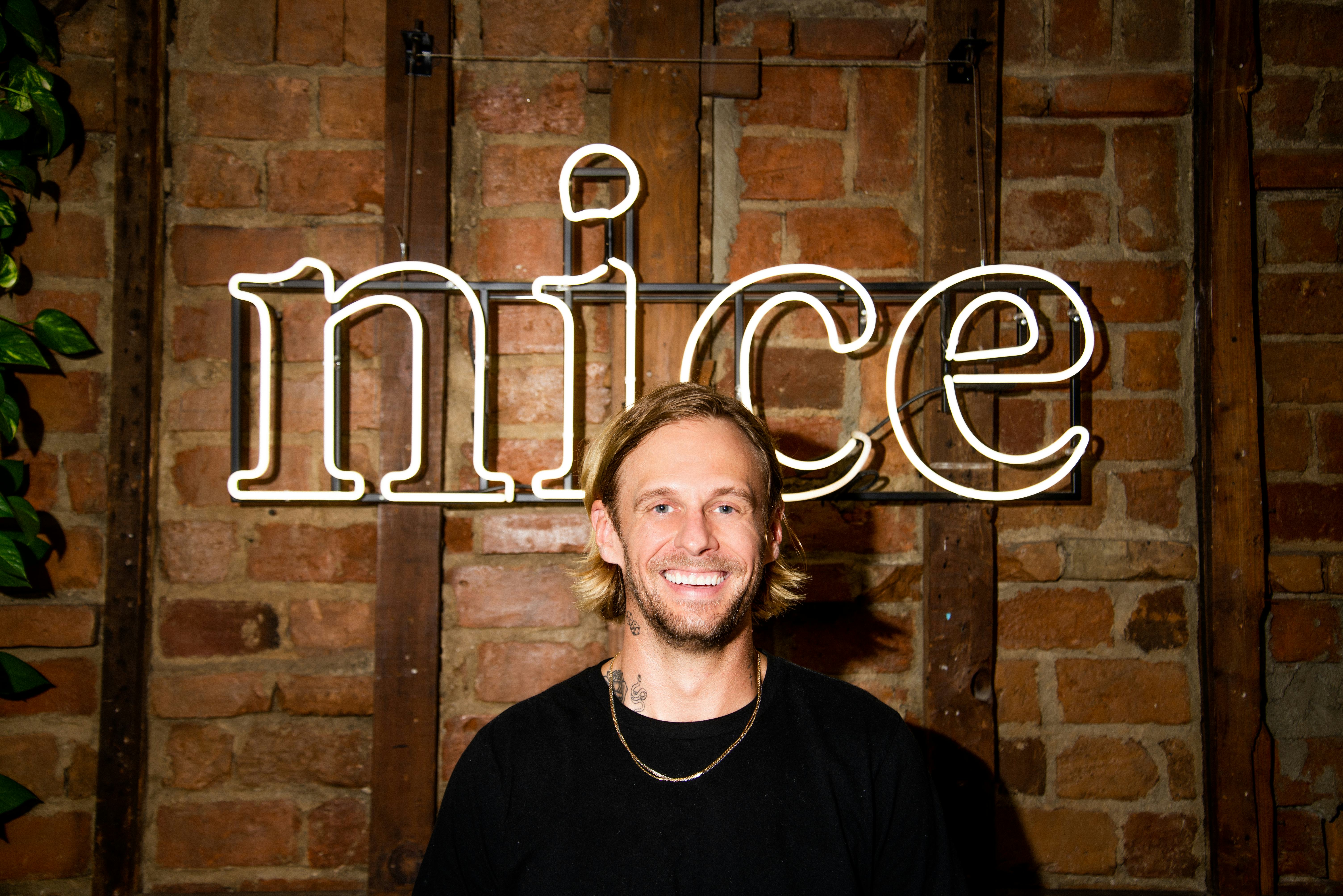 Foreverist founder Robert Boyle standing in front of a &ldquo;Nice&rdquo; neon sign inside his tattoo studio Nic&hellip;