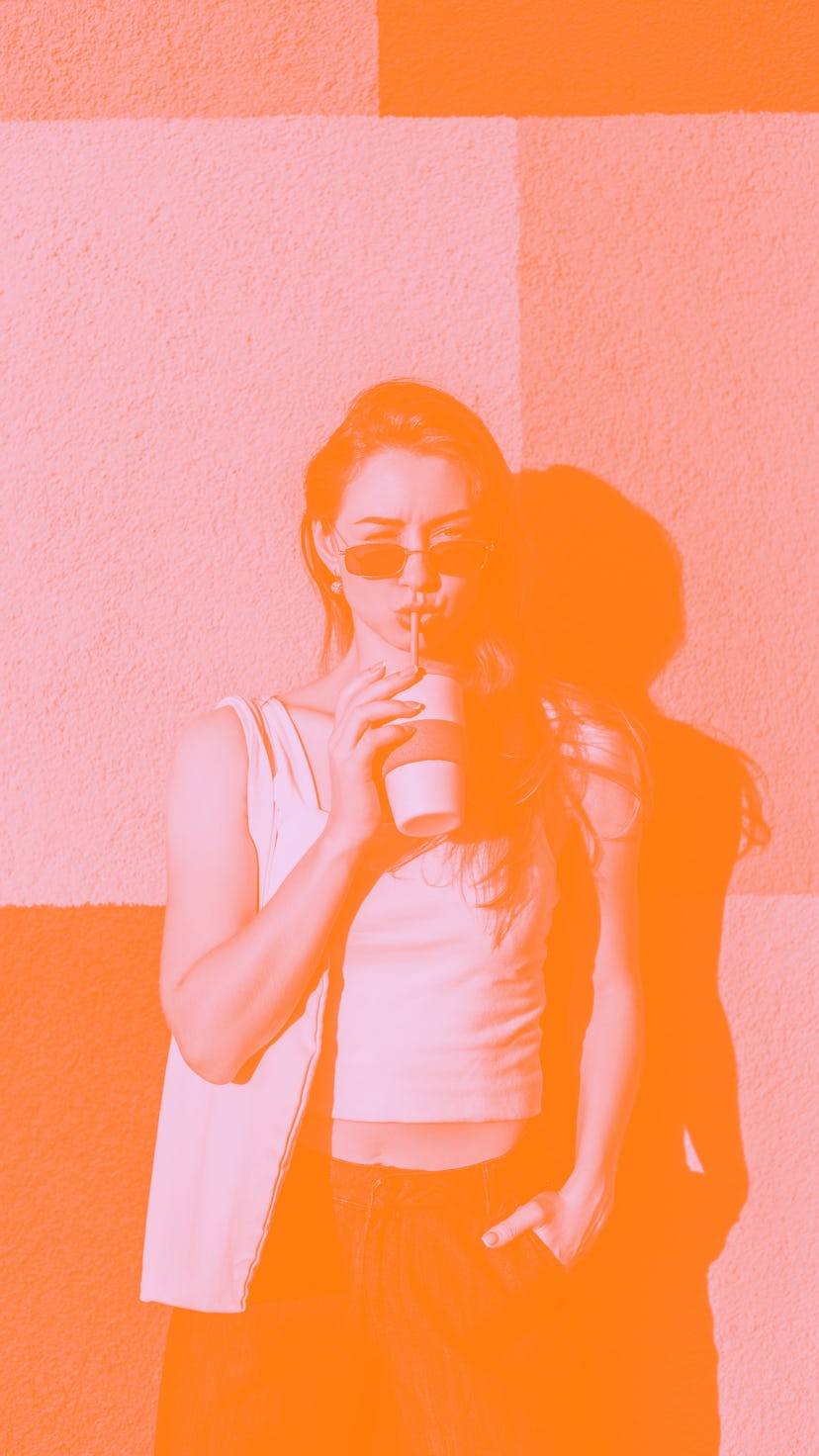 Young woman drinking a pumpkin spice latte outside, because her zodiac sign's obsessed with PSLs.