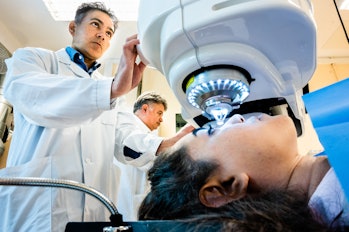 A woman lying down on exam table has a machine with a bright light directed into her eye 