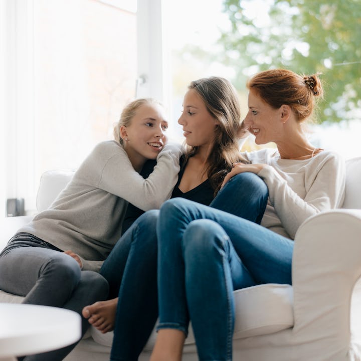 Three siblings sit together on a couch, with the youngest and oldest staring at the middle child.