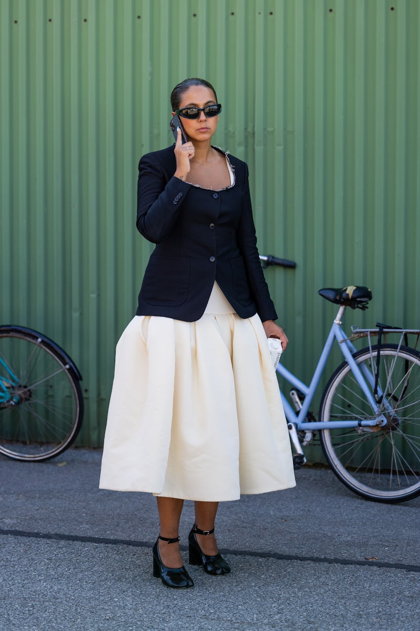 A woman wearing a wide white dress, black open chest blazer, dark glasses and heeled shoes during Co...