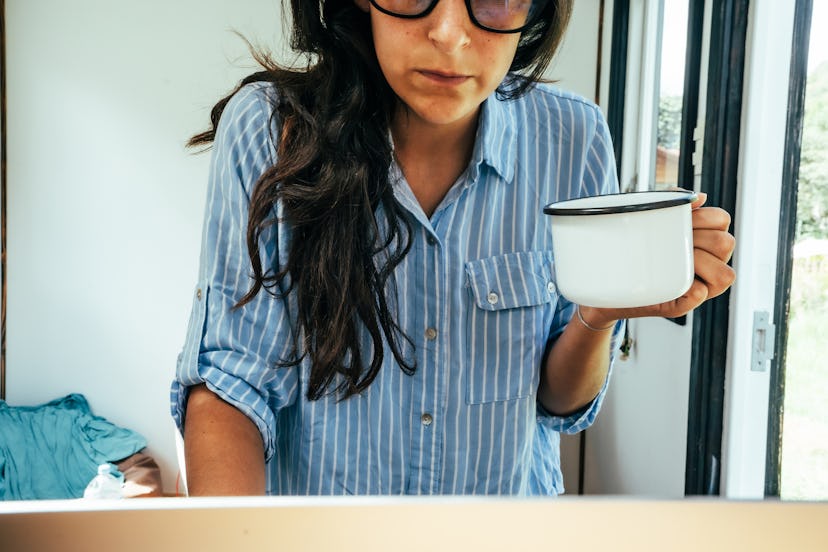 A woman in the shirt leaning on a desk while holding a cup of coffee