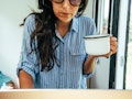 A woman in the shirt leaning on a desk while holding a cup of coffee