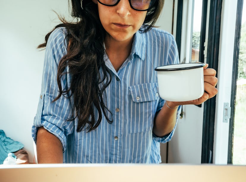 A woman in the shirt leaning on a desk while holding a cup of coffee