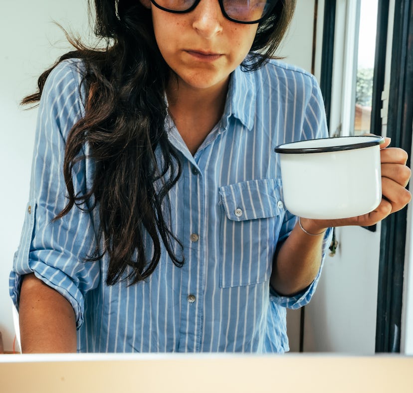 A woman in the shirt leaning on a desk while holding a cup of coffee