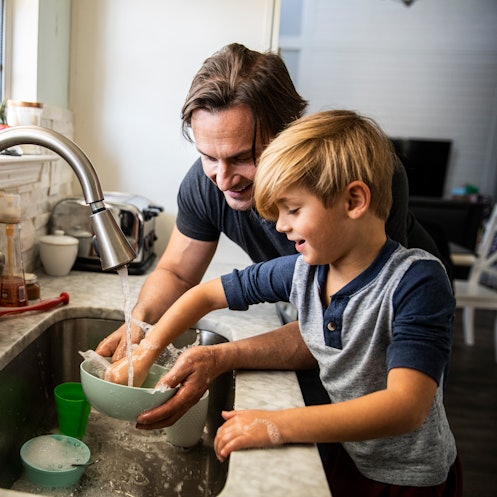 A dad helps his son with ADHD do dishes at the sink.
