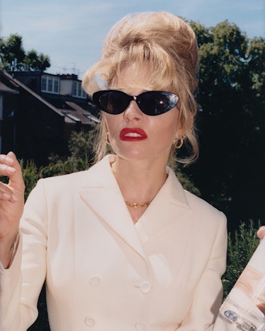 A closeup of Sienna Miller holding a bottle and cigarette in a white blazer and black sunglasses 