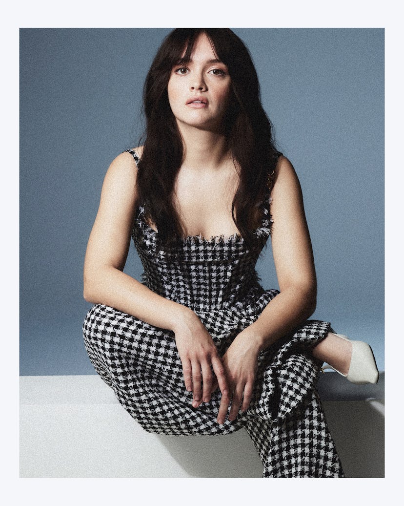 Olivia Cooke posing in a checkered jumpsuit and white heels