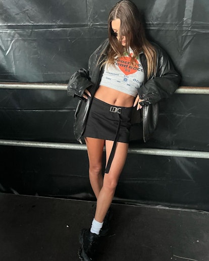 hailey bieber wearing a black mini skirt with a cropped tee, an oversized leather jacket and white s...