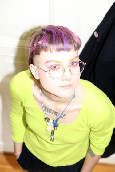 A person with purple hair wearing a fluorescent yellow shirt