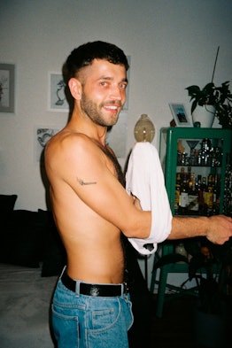 A shirtless person putting on a white shirt