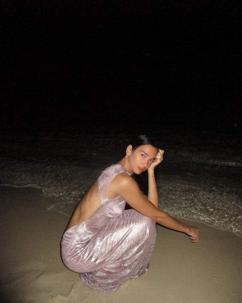 dua lipa models a long light pink lamé missoni dress featuring an open back on a beach at night