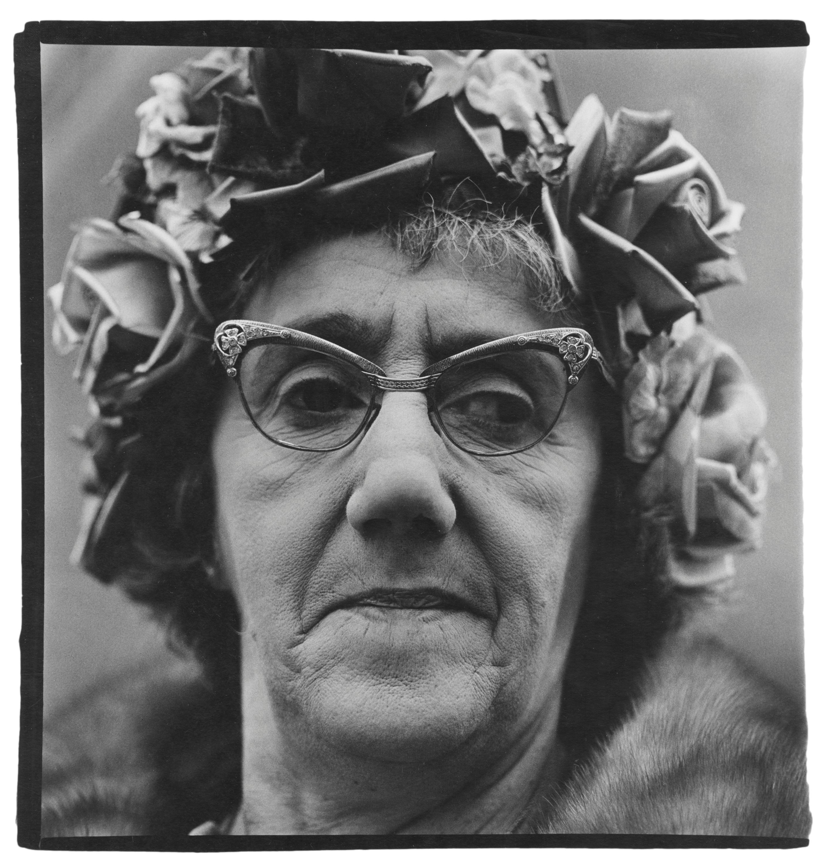A closeup portrait of a woman wearing a hat with roses and statement glasses