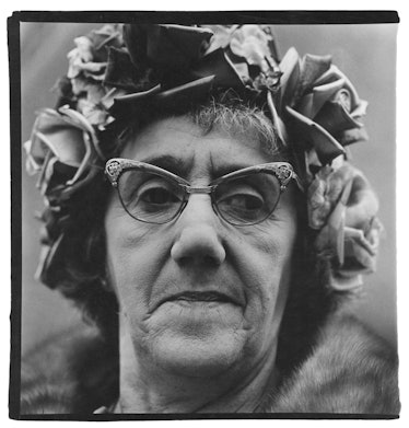 A closeup portrait of a woman wearing a hat with roses and statement glasses