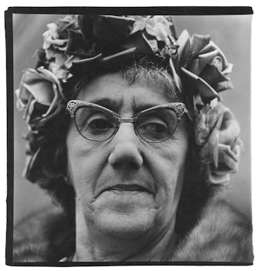 A close up portrait of a woman wearing a hat with roses and statement glasses