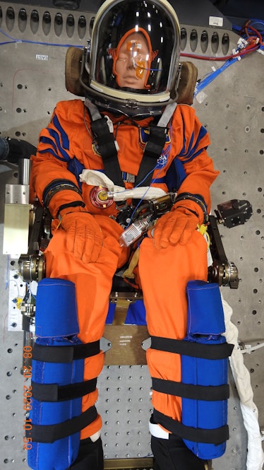 A mannequin in an orange astronaut suit sitting. 